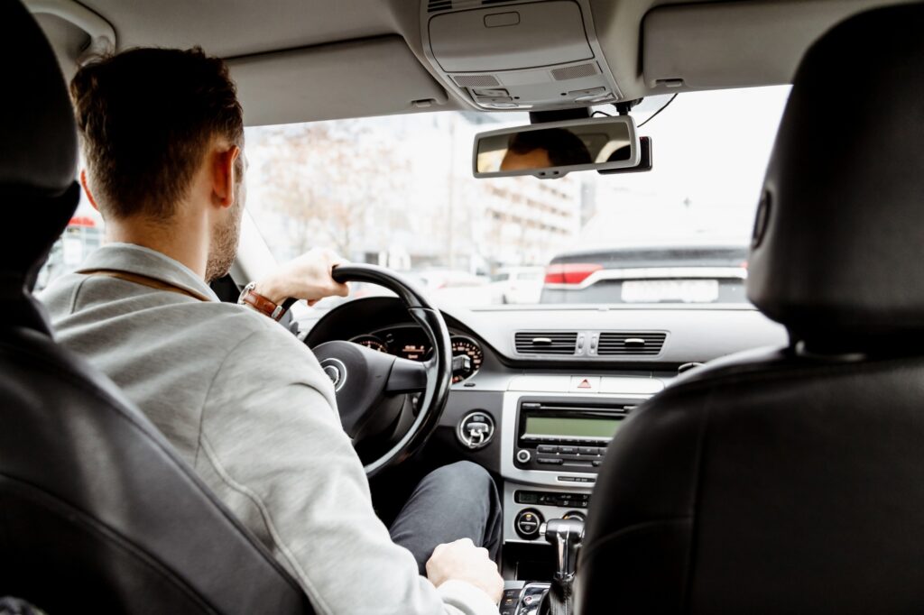 Man in suit driving a car, personal driver, business taxi, back view from saloon